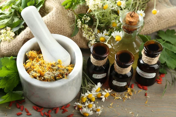 Herbes, baies et fleurs au mortier, sur fond de table en bois — Photo