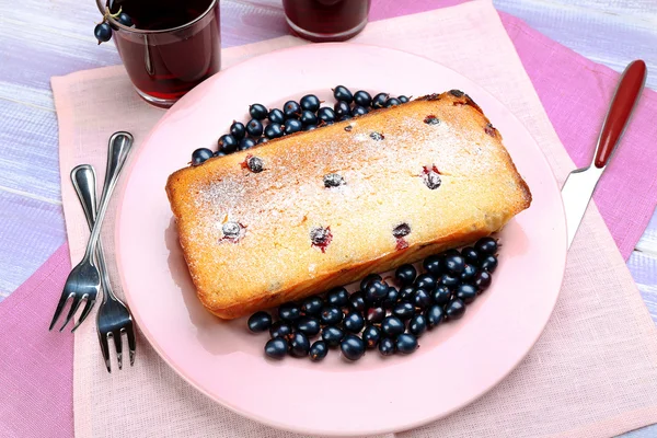 Freshly baked cake with black currants in pink plate on wooden table, top view