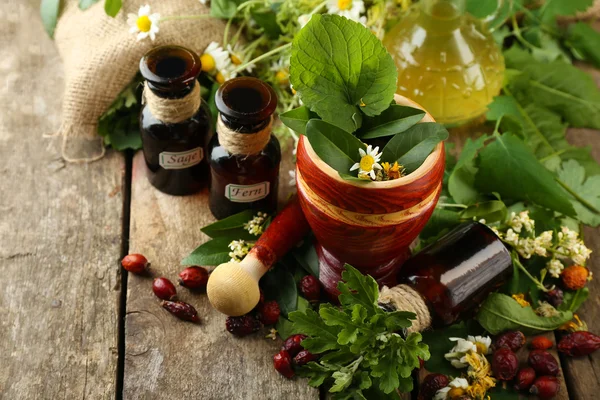 Herbes, baies et fleurs au mortier, sur fond de table en bois — Photo