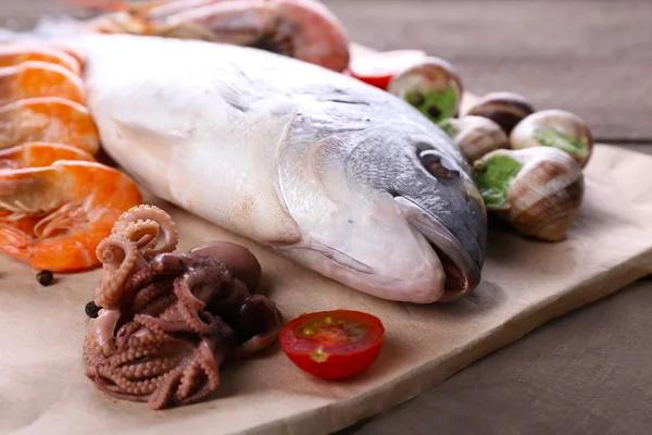 Dorado fisk och andra ingredienser på pergament på träbord, närbild — Stockfoto