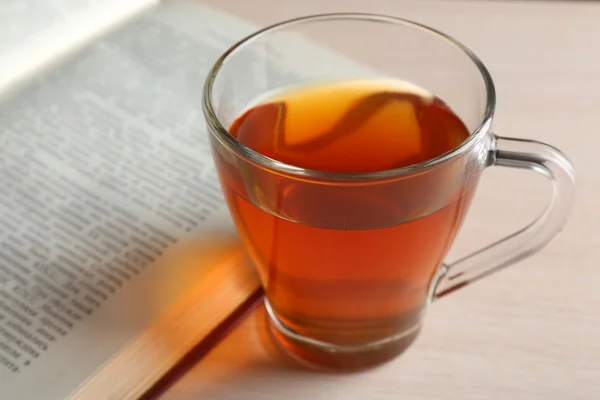 Coupe de thé en verre avec livre ouvert sur table en bois, gros plan — Photo