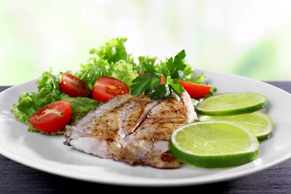 Plato de filete de pescado con ensalada y lima sobre fondo brillante —  Fotos de Stock