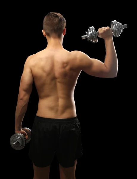 Muscle young man holding dumbbells on dark background — Stock Photo, Image