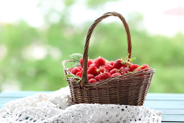 Fresh raspberries in wicker basket on wooden table on blurred nature background — Stock Photo, Image