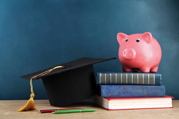 Piggy bank a könyvek és a Grad kalap tábla háttér — Stock Fotó