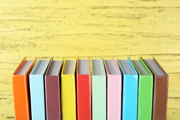 Livros coloridos sobre fundo de madeira amarelo — Fotografia de Stock