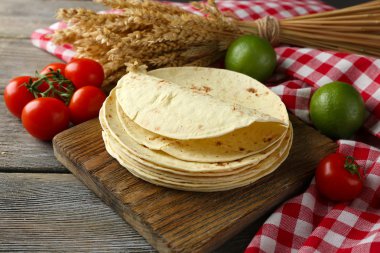 Ev yapımı kepekli un tortilla ve ahşap masa arka plan üzerinde kesme tahtası üzerinde sebze yığını