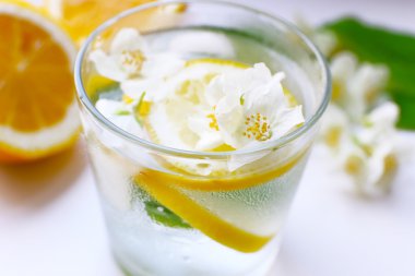 Bardak soğuk ferahlatıcı yaz içeceği çiçekli ve masada limon dilimleri kapat