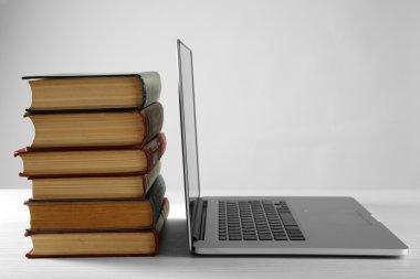 Gri arka plan üzerinde dizüstü bilgisayar ile kitap yığını