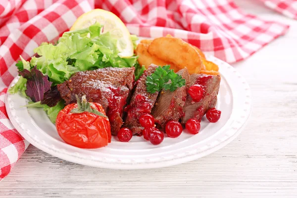 Tasty roasted meat with cranberry sauce and roasted vegetables on plate, on color wooden background — Stock Photo, Image