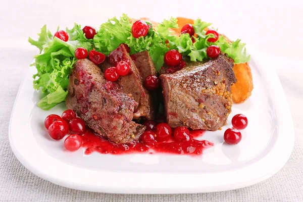 Вкусное жареное мясо с клюквенным соусом на тарелке, на светлом фоне — стоковое фото