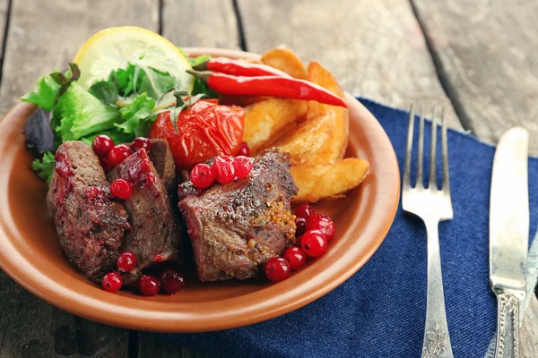 Tasty roasted meat with cranberry sauce, salad and roasted vegetables on plate, on wooden background