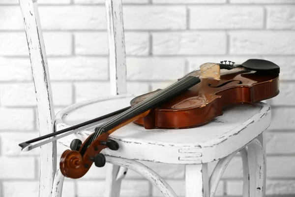 Скрипка на стуле, на кирпичном фоне стены — стоковое фото