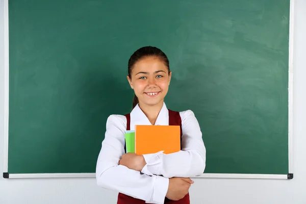 Hermosa niña de pie cerca de pizarra en el aula —  Fotos de Stock