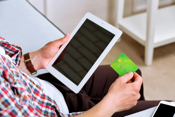 Homem segurando cartão de crédito e tablet no sofá no quarto — Fotografia de Stock