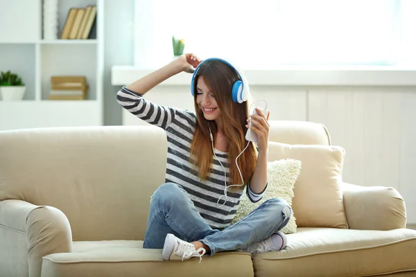 Woman listening music in headphones while sitting on sofa in room — Stock Photo, Image