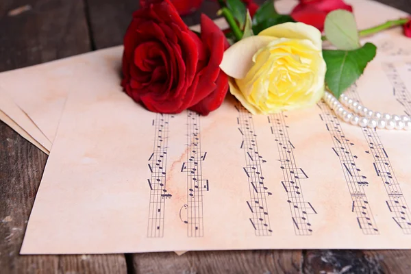 Beautiful roses with pearls on music sheets on wooden table, closeup — Stock Photo, Image