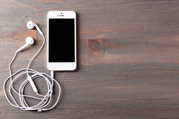 Téléphone portable et écouteurs sur fond en bois — Photo