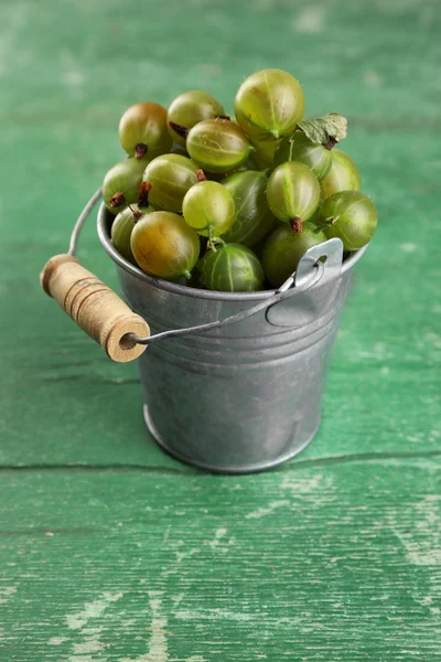 Uva spina verde in secchio su sfondo di legno — Foto Stock