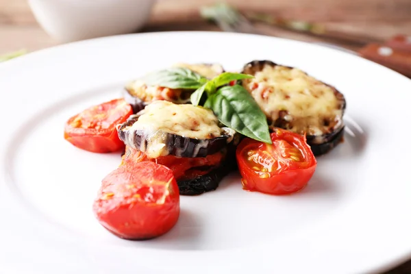 Prato de berinjela com tomates cereja e queijo em placa branca sobre mesa de madeira, close-up — Fotografia de Stock
