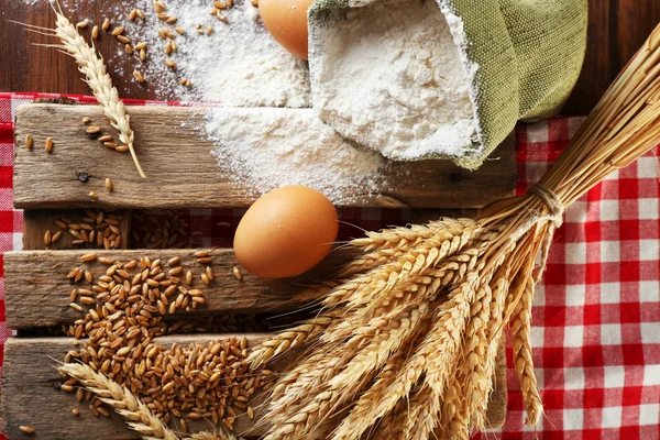 Whole flour with wheat and eggs on wooden table, closeup — Stock Photo, Image