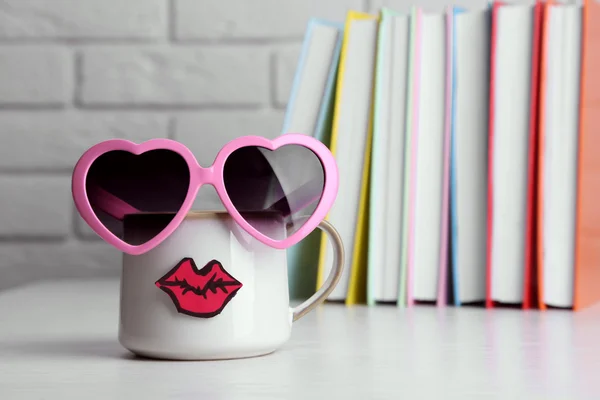 Boeken en cup met lippen op houten tafel op bakstenen muur achtergrond — Stockfoto