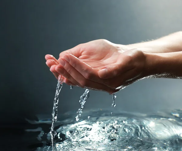 Vrouwelijke handen met water spatten op donkere achtergrond — Stockfoto