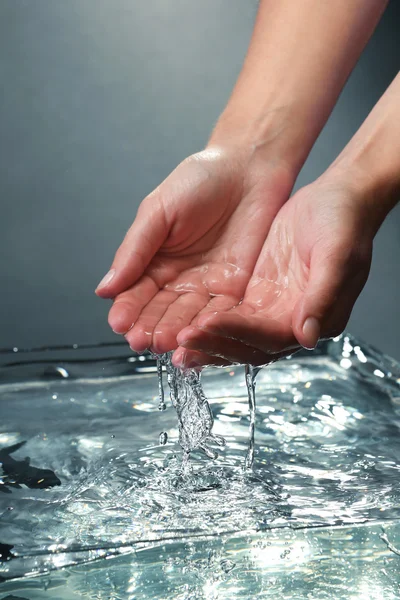 Mains féminines avec éclaboussures d'eau sur fond sombre — Photo