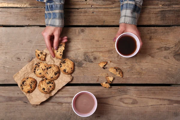 Female hands holding cup of coffee and cookies on wooden table close up — Stock Photo, Image