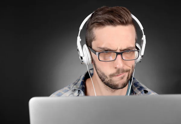 Jovem bonito com laptop no fundo cinza — Fotografia de Stock