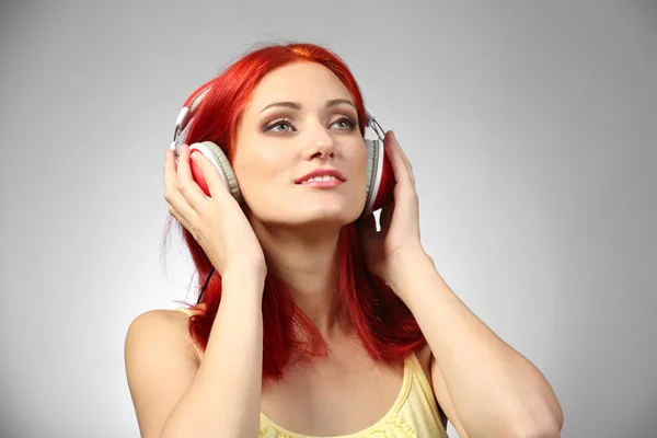 Mulher bonita com fones de ouvido no fundo cinza — Fotografia de Stock
