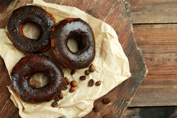 Delicious doughnuts with chocolate icing and coffee beans on table close up — Stock Photo, Image