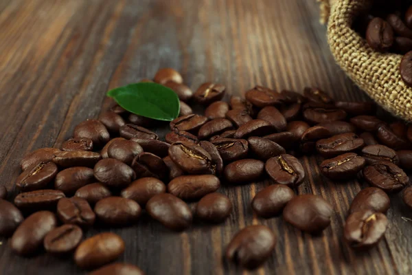 Кофейные зёрна с листьями на деревянном столе — стоковое фото