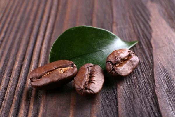 Coffee beans with leaf on wooden background — Stock Photo, Image