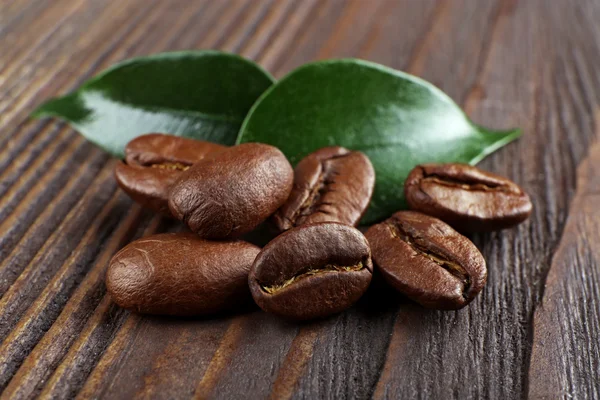 Grains de café avec des feuilles sur fond en bois — Photo