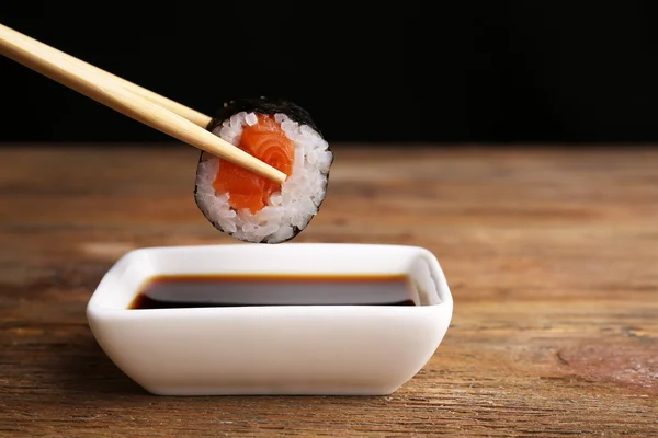 Dipping roll in sauce on dark background — Stock Photo, Image