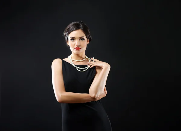 Hübsche Frau in schwarzem Kleid und weißen Perlen auf dunklem Hintergrund — Stockfoto