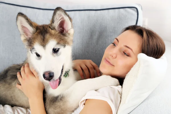 Mulher deitada com seu cão malamute no sofá no quarto — Fotografia de Stock