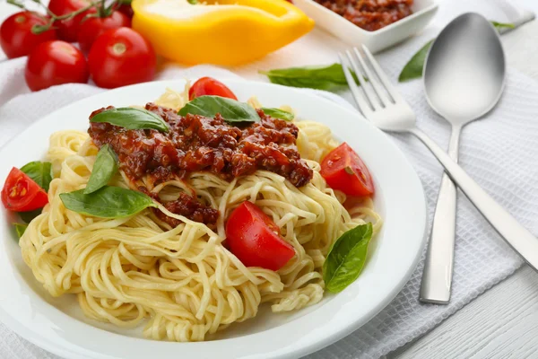 Spaghetti alla bolognese su piatto bianco, su fondo di legno a colori — Foto Stock