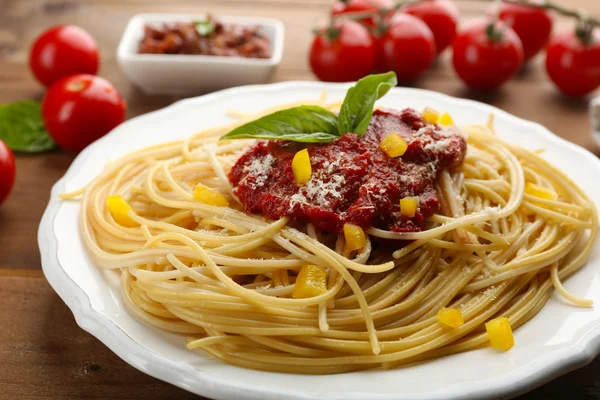 Espaguete com molho de tomate, páprica e queijo na placa branca, na cor de fundo de madeira — Fotografia de Stock
