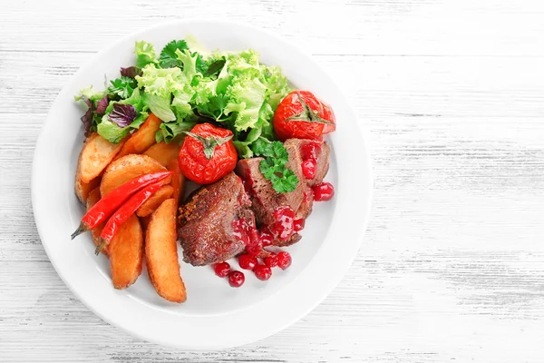 Smaczne mięso pieczone z sosem żurawinowym i pieczone warzywa na talerzu, na tle drewniane kolor — Zdjęcie stockowe