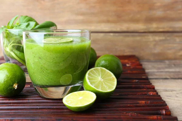 Vaso de jugo verde saludable con albahaca y limas en la mesa de cerca — Foto de Stock