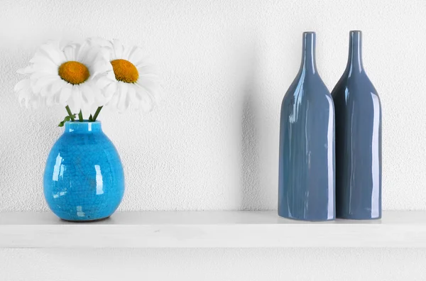 Декоративные вазы с цветами на деревянной полке на белом фоне обоев — стоковое фото