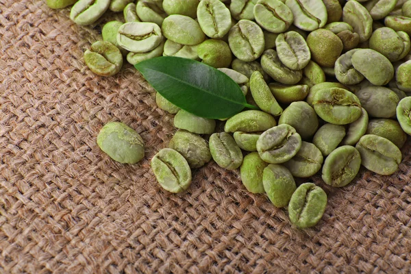 Купка зелених кавових зерен з листям на мішечку крупним планом — стокове фото