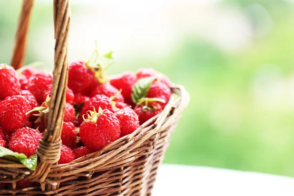 在木制的桌子上模糊的自然背景上的柳条篮子里的新鲜树莓 — 图库照片