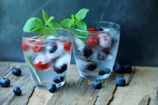 Bicchieri di bevanda estiva rinfrescante fredda con bacche e cubetti di ghiaccio sul tavolo da vicino — Foto Stock