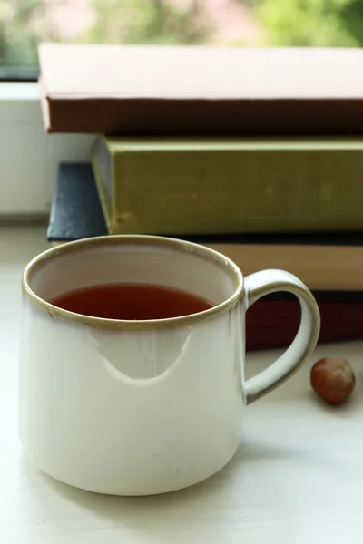 Tasse de thé avec pile de livres sur le rebord de la fenêtre, gros plan — Photo