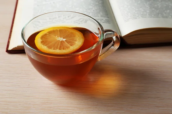 Glass cup of tea with book on wooden table, closeup — Stock Photo, Image