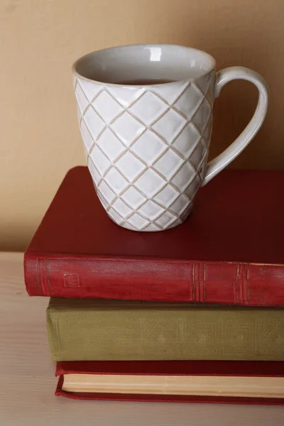 Bardak çay ışık duvar arka plan üzerinde ahşap masa üzerinde kitap yığını ile — Stok fotoğraf