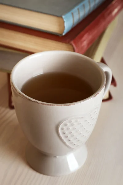 Taza de té con pila de libros sobre mesa de madera sobre fondo de pared claro —  Fotos de Stock
